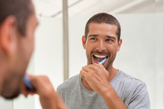 man smiling while brushing his teeth