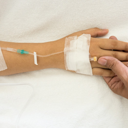 Child receiving IV sedation while holding mom’s hand