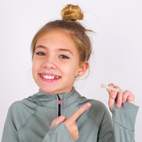 Teen girl smiling while pointing to Invisalign aligner