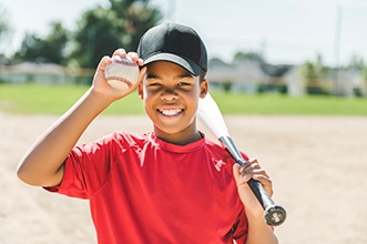 Smiling child holding baseball and bat on field