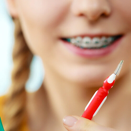 Girl with braces holding toothbrush and flosser